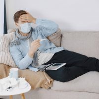 Sick guy in living room. Middle age man feeling sick with cold and fever at home. Man in a medical mask.